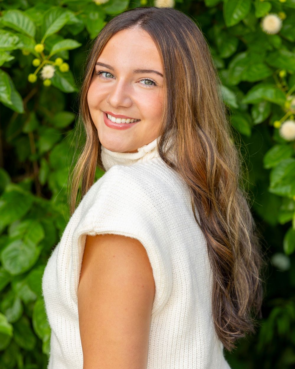 Portrait photo against lush green foliage background showing bright smile and casual summer style.