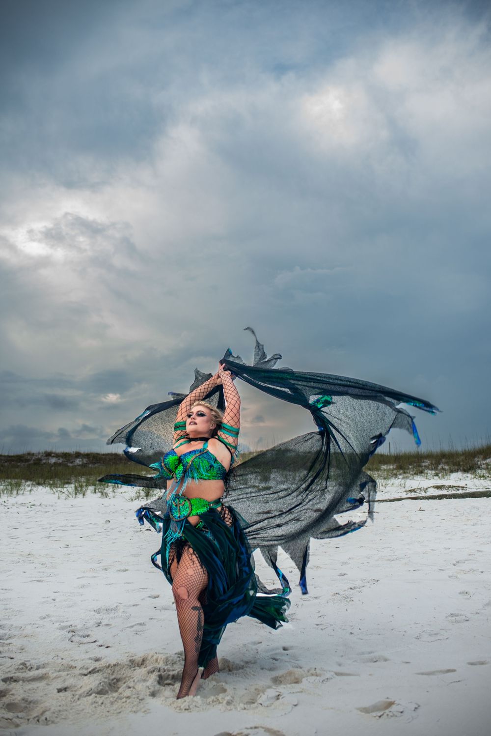 Black fabric billows dramatically in the wind on a white sand beach under stormy clouds at dusk.