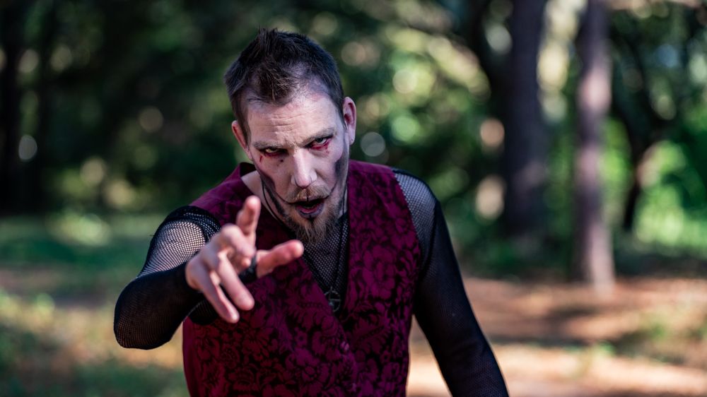 A person in dark clothing aims a handgun during an outdoor shooting practice session in a wooded area.