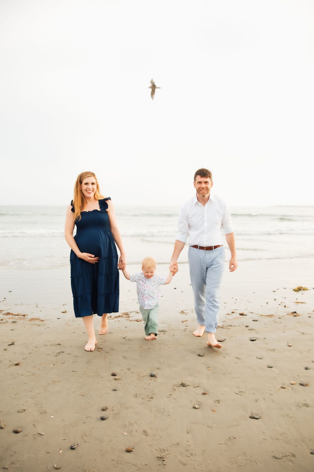 Pregnant woman in navy dress walks on beach with toddler and man in white shirt, ocean waves in background. Second Beach Middletown, RI