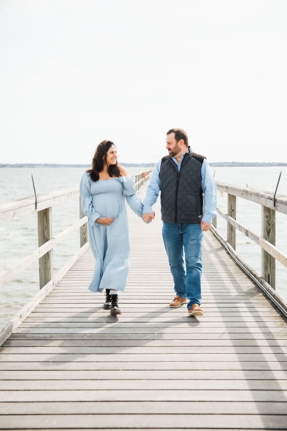 Pregnant couple holding hands and walking on a wooden pier over calm water. maternity photoshoot, Beavertail Jamestown RI