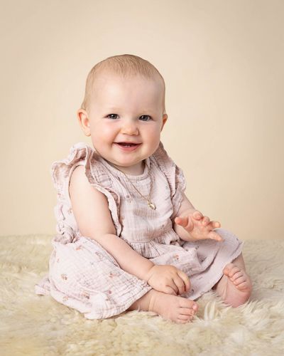 A collection of portraits featuring a baby in a light pink dress sitting on a cream-colored fluffy rug.