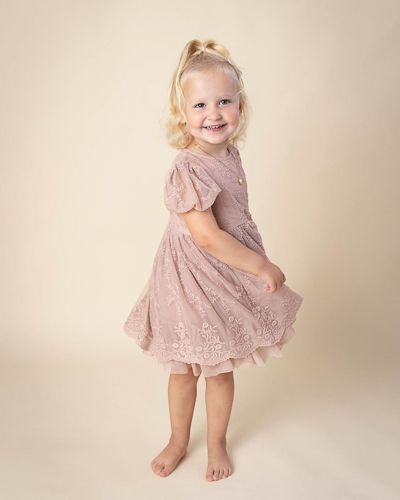 A young child in a sparkly pink dress twirls and plays in a studio setting with a neutral backdrop.