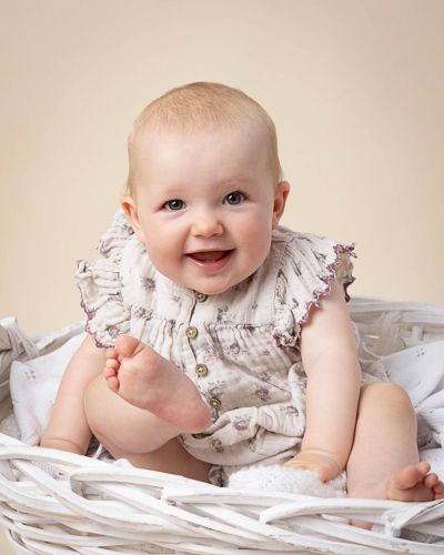Baby in ruffled white outfit lying on soft bedding with a delightful smile.