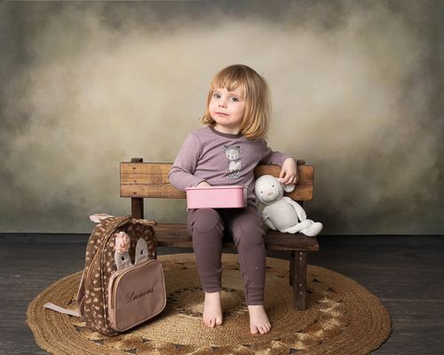 A girl sits on a bench on a round jute rug with a white bunny, creating a cozy scene against a moody dark backdrop.