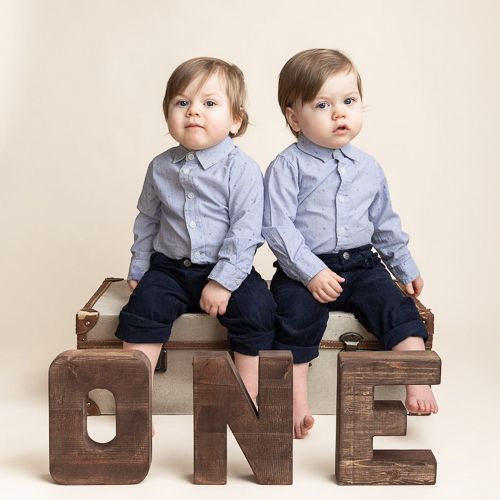 twin boys sitting on wooden block letters spelling ONE for first birthday photoshoot.