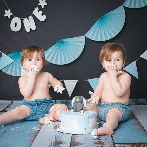 Cake smash photo series with blue decorations and white cake against dark background.