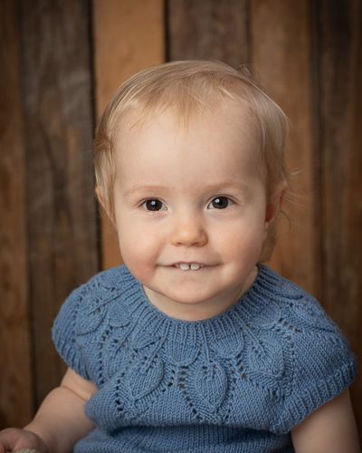 Baby wearing blue knit dress poses in front of rustic wood background in series of portraits.