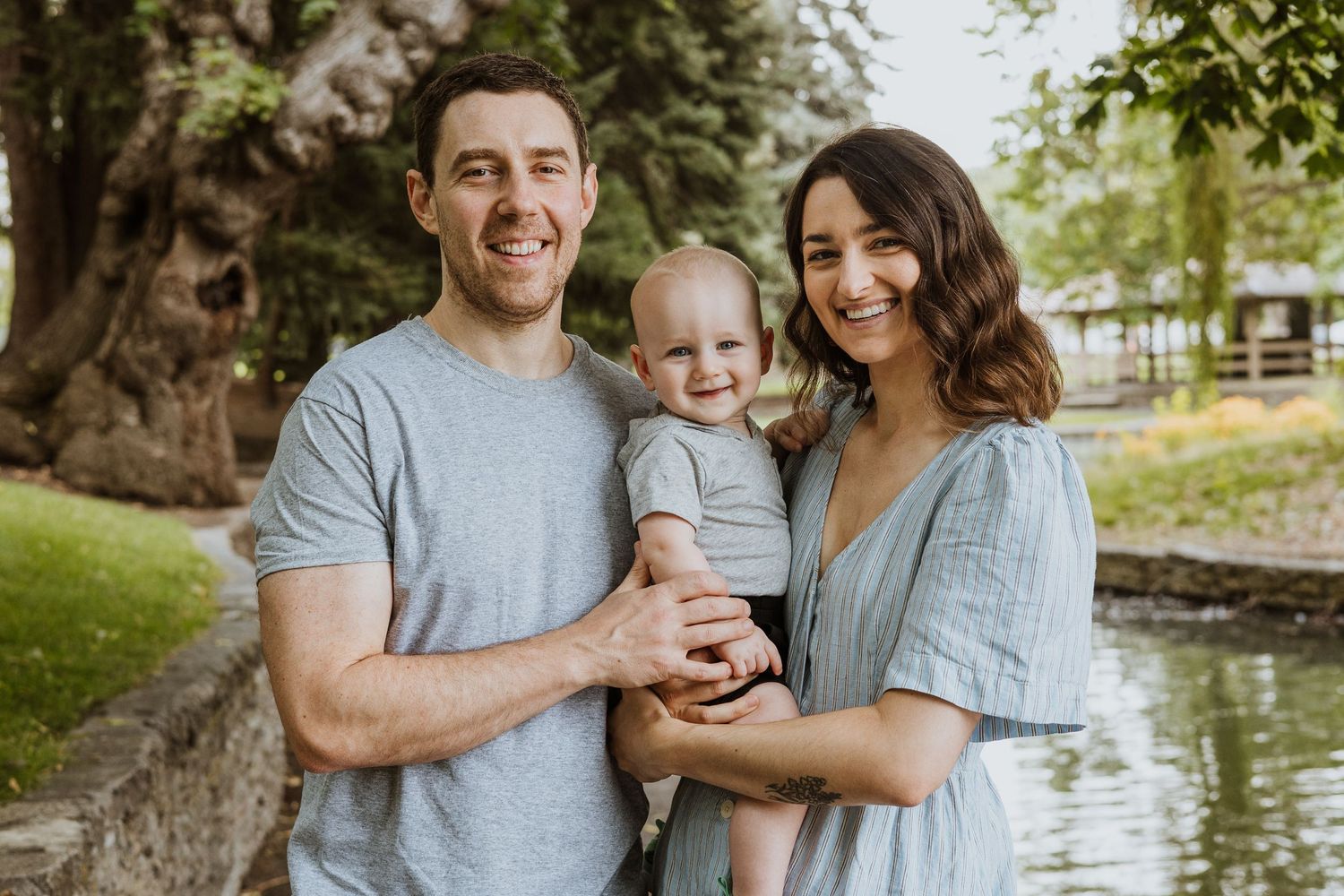 a family of three including one small child sitting in a sunny field smiling at the camera