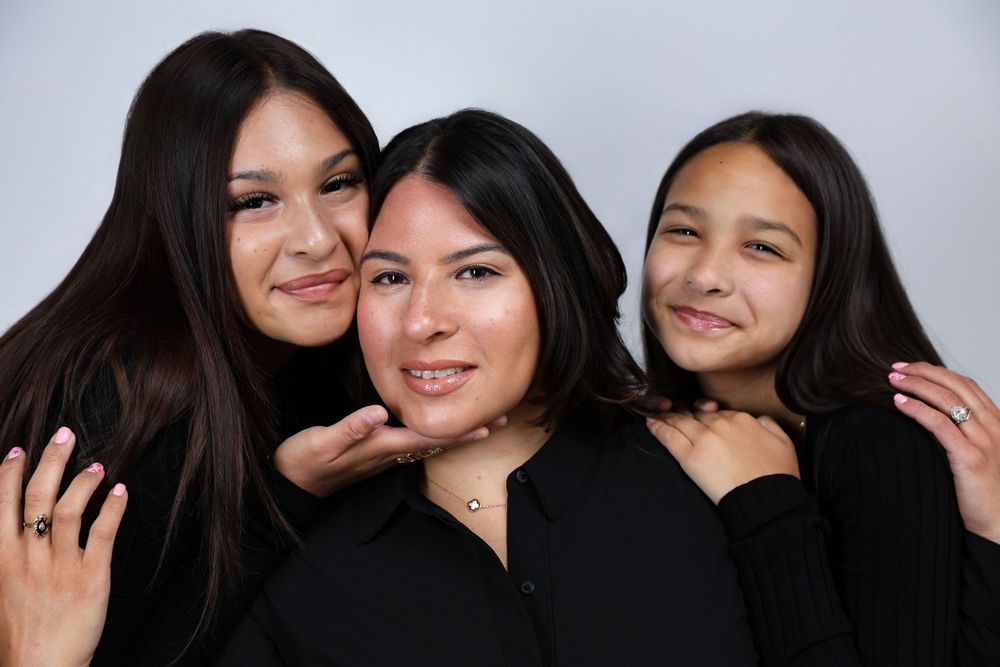 Three young women in black tops smiling together in casual studio portrait.
