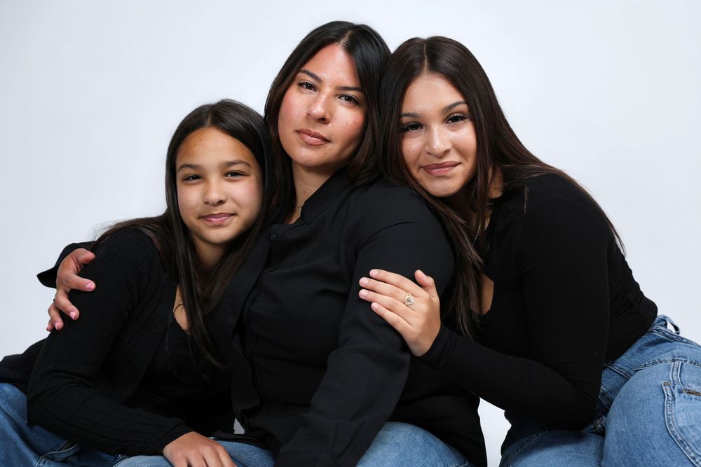 Two friends in matching black sweaters and jeans pose playfully together against a white backdrop.