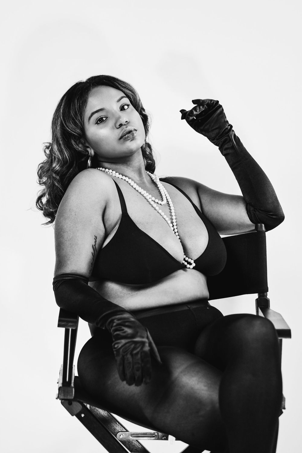Classic black and white portrait with pearl necklace and gloves in director's chair styling.