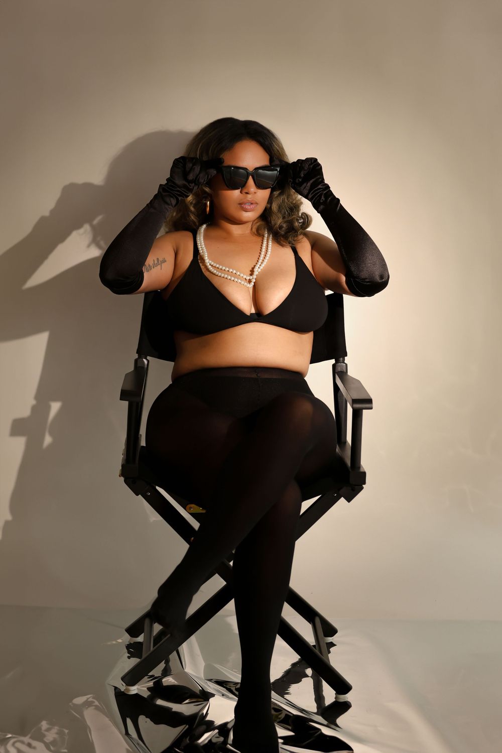 Fashion portrait featuring black lingerie, long gloves and pearl necklace on director's chair.