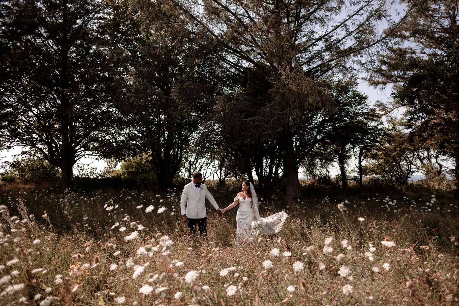 Wedding guests toss confetti in celebration outdoors under a bright sky.