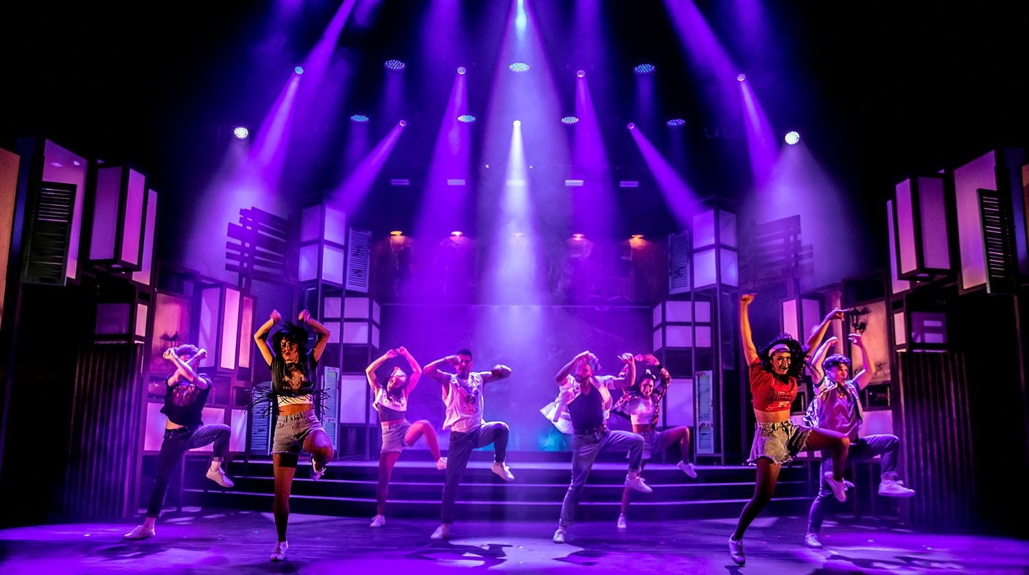 Dancers perform energetic choreography on stage with purple lighting and modern set design.
