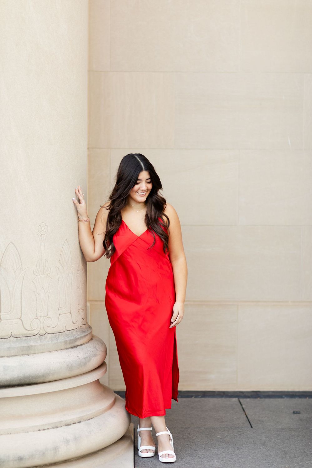 Figure in flowing red dress poses elegantly against classical column architecture.