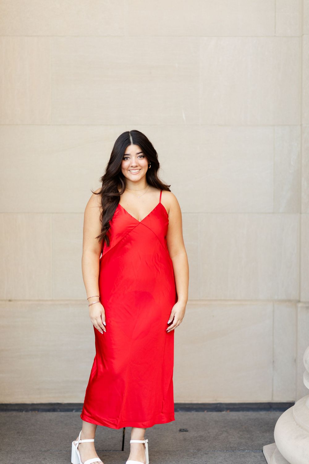 Person wearing red slip dress and sneakers poses with column against neutral wall.