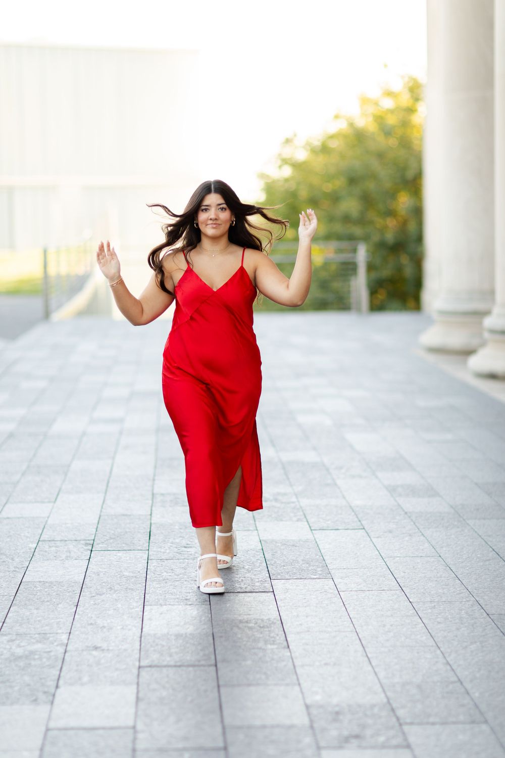 Person dancing joyfully in a flowing red dress against a backdrop of classical architecture.