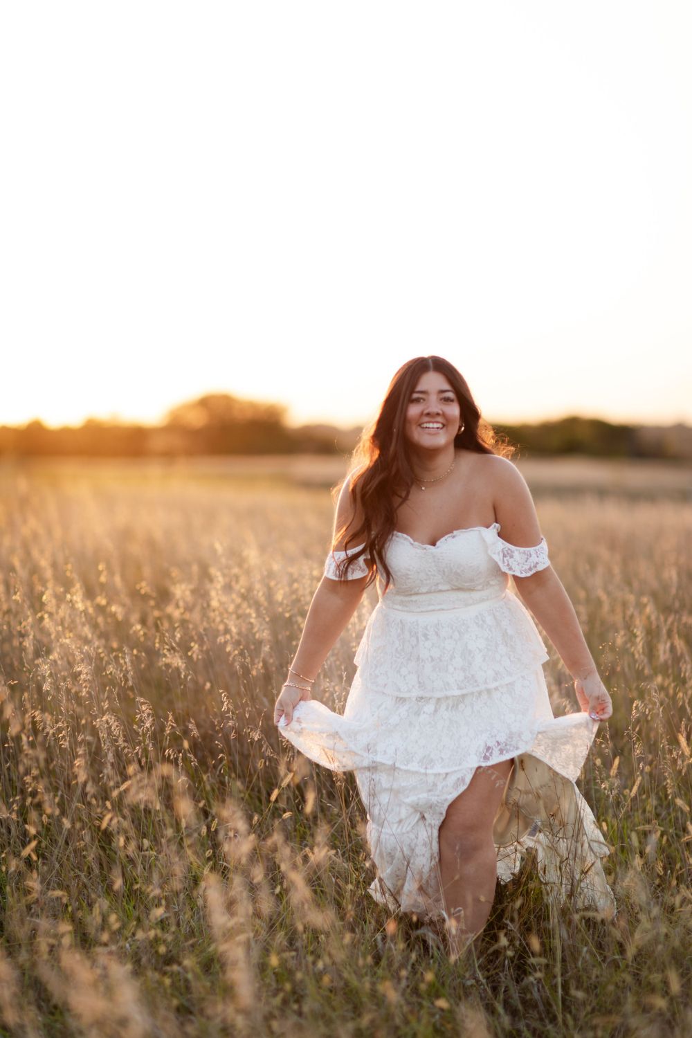 Figure in an ethereal white dress poses elegantly in a sunlit field of tall grass.