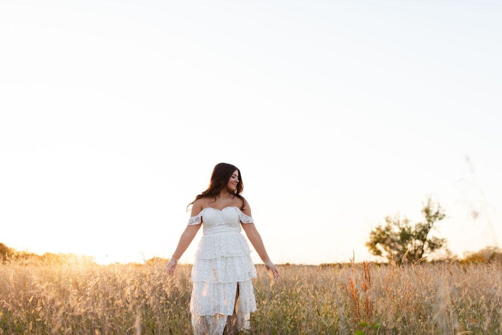 Person in a flowing white dress poses against a golden sunset in a wild meadow.