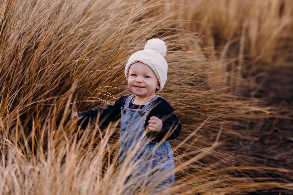 Beautiful image of Baby in sand dune grass smiling - Taranaki family photographer.