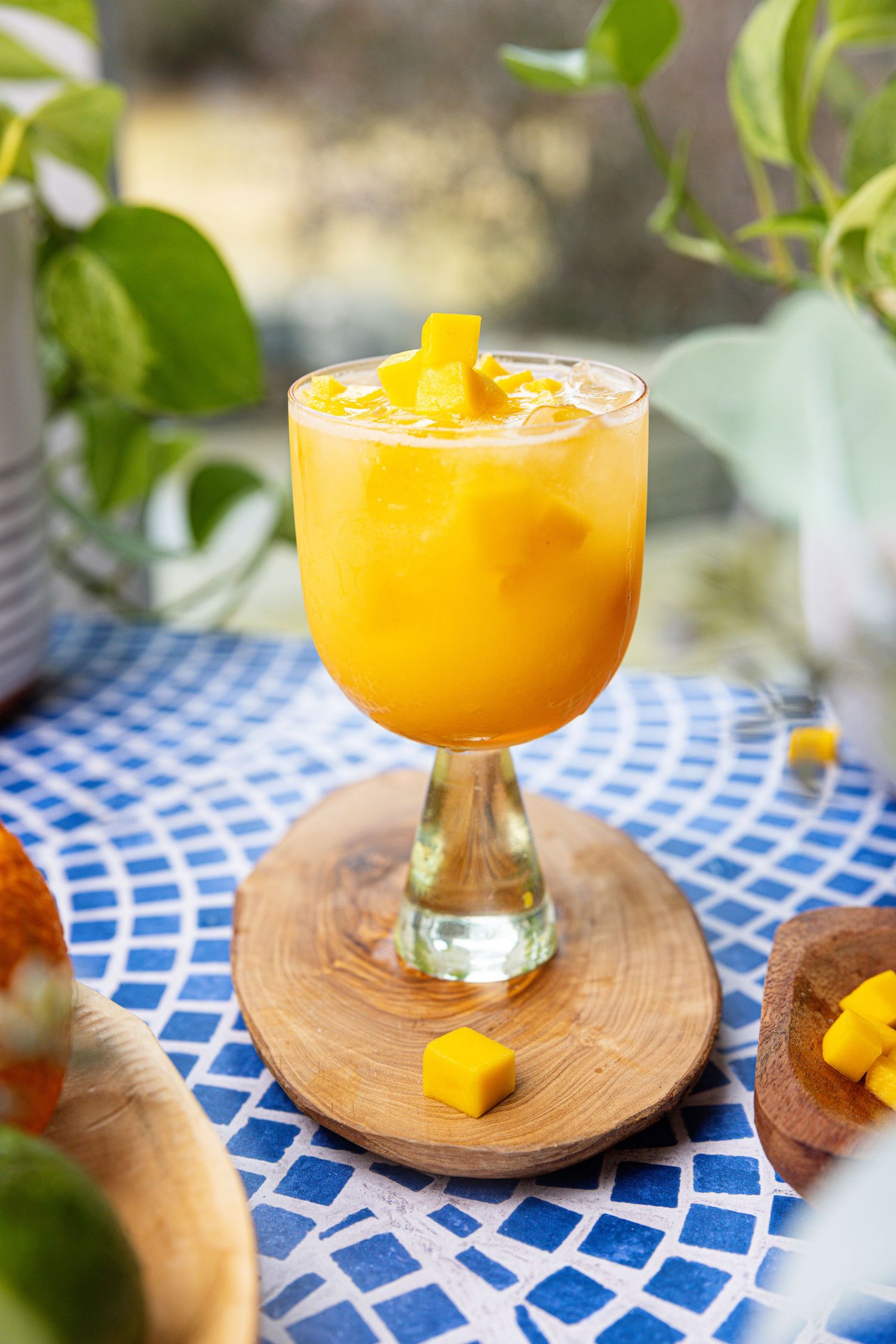 Vibrant mango cocktail in a stemmed glass garnished with fresh mango chunks on a blue table.