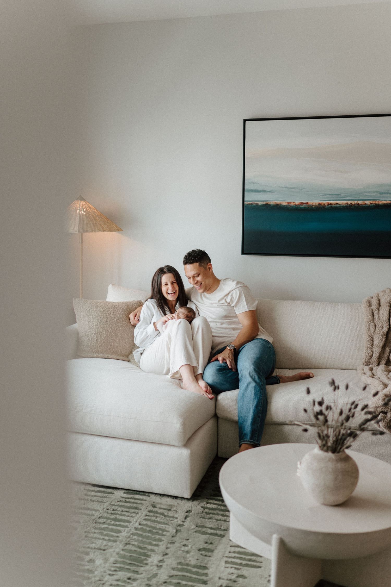 A couple relaxes on white couch beneath coastal artwork in modern living room.