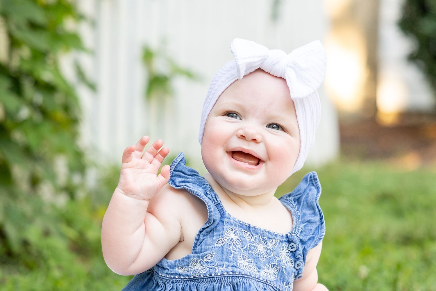 A baby girl smiles and waves in a white headband at Historic Oak View Park family photos /
