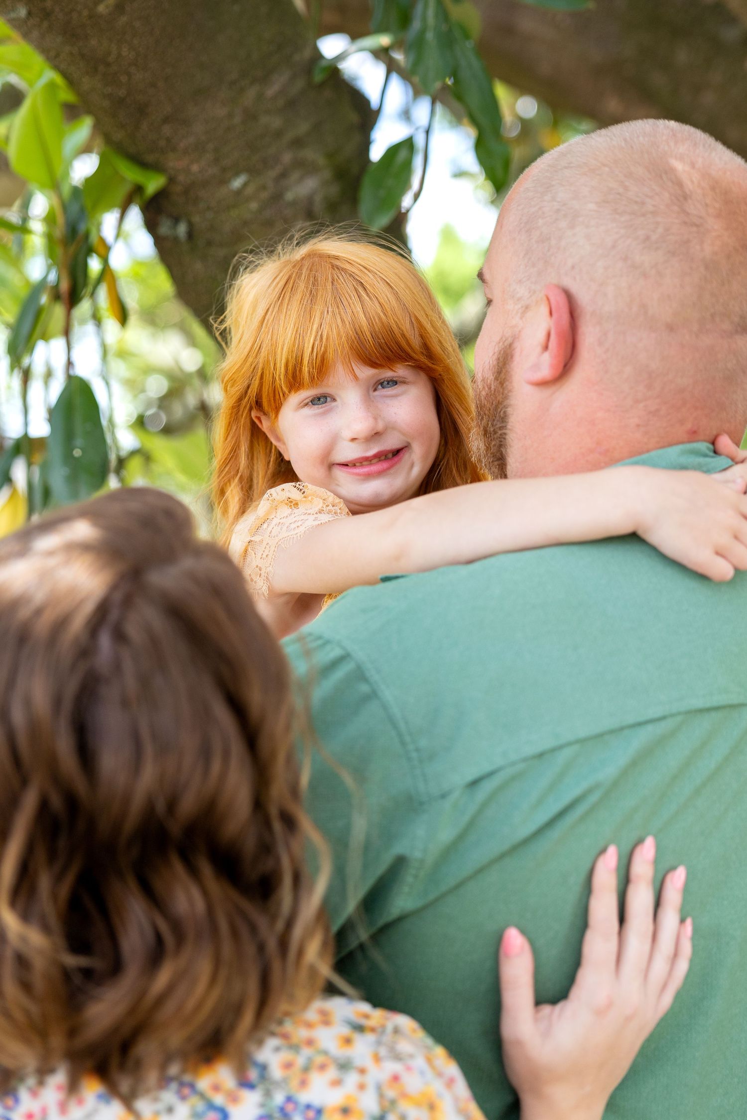 A red head girl smiles over her parent's shoulders in her Clayton, NC family photos.