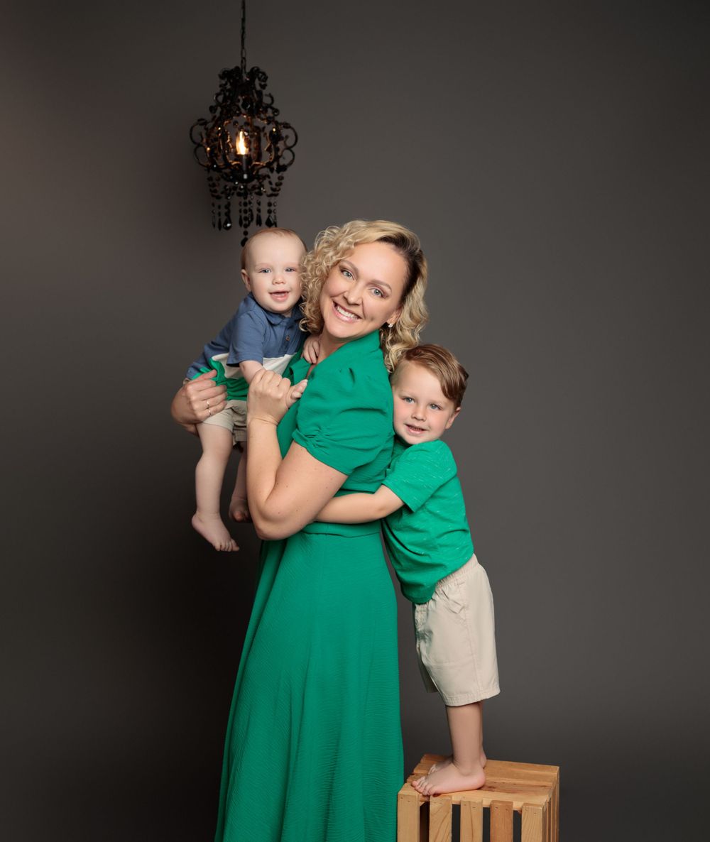 A loving family group portrait against a dark backdrop, with matching emerald green outfits and a decorative hanging lamp above.