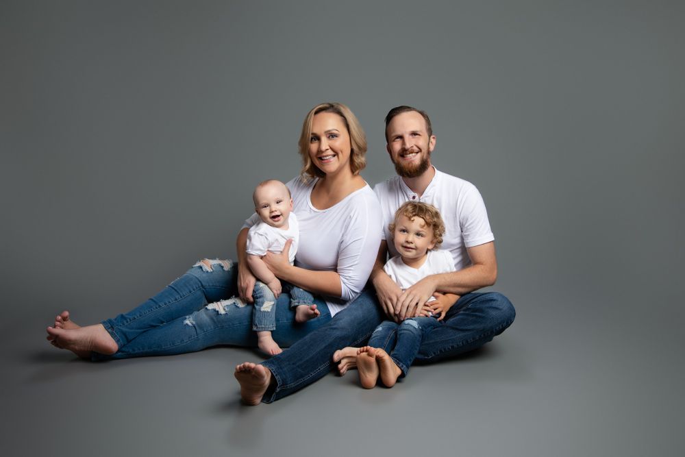 A family wearing matching denim and white sits together on a gray studio floor.