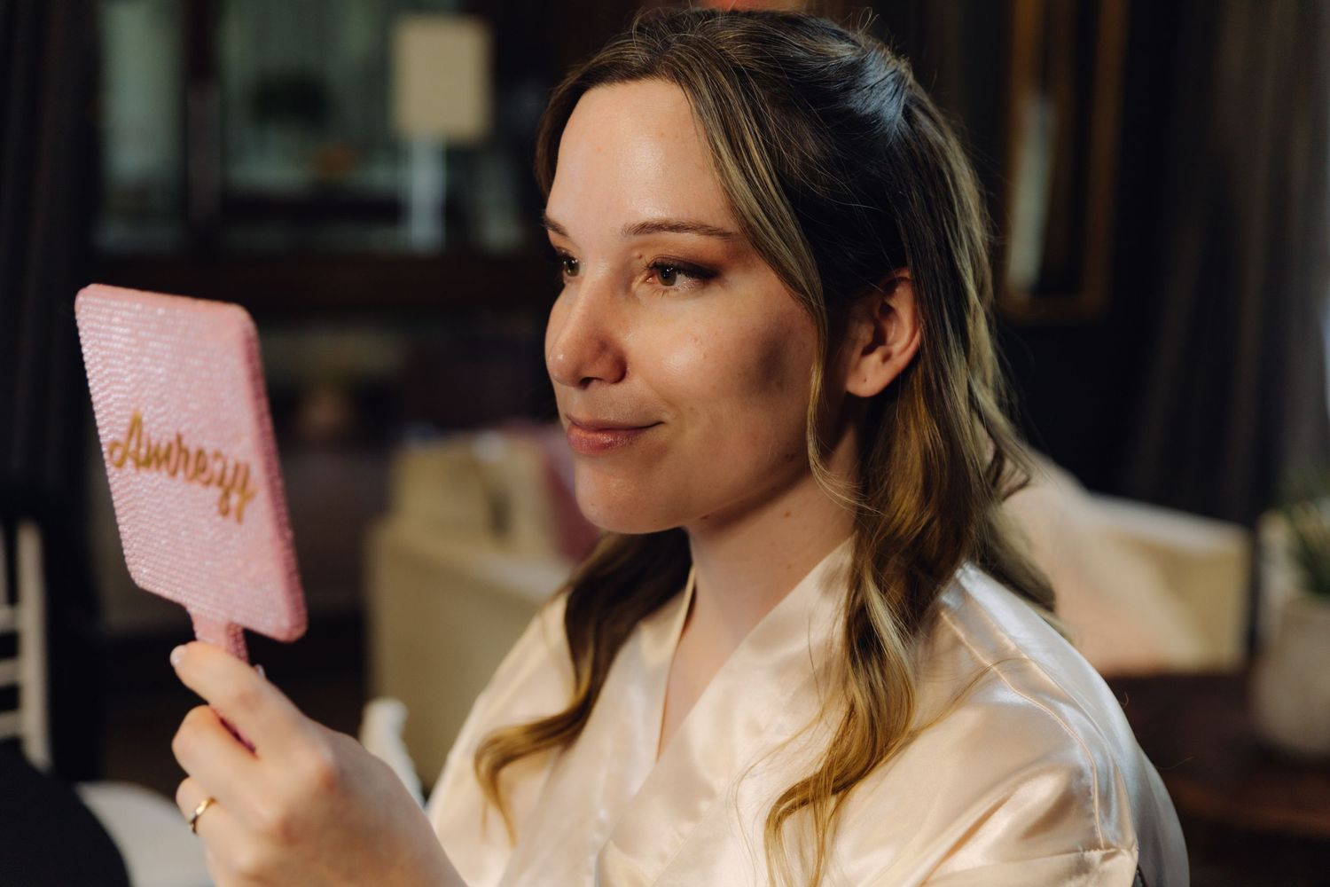 Bride admiring pink personalized hand mirror during wedding day preparations.