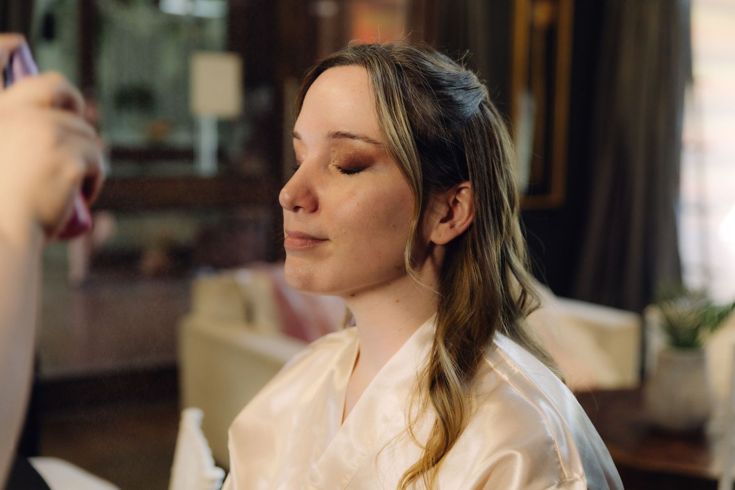 Bride having makeup applied by artist during wedding day preparations in white robe.