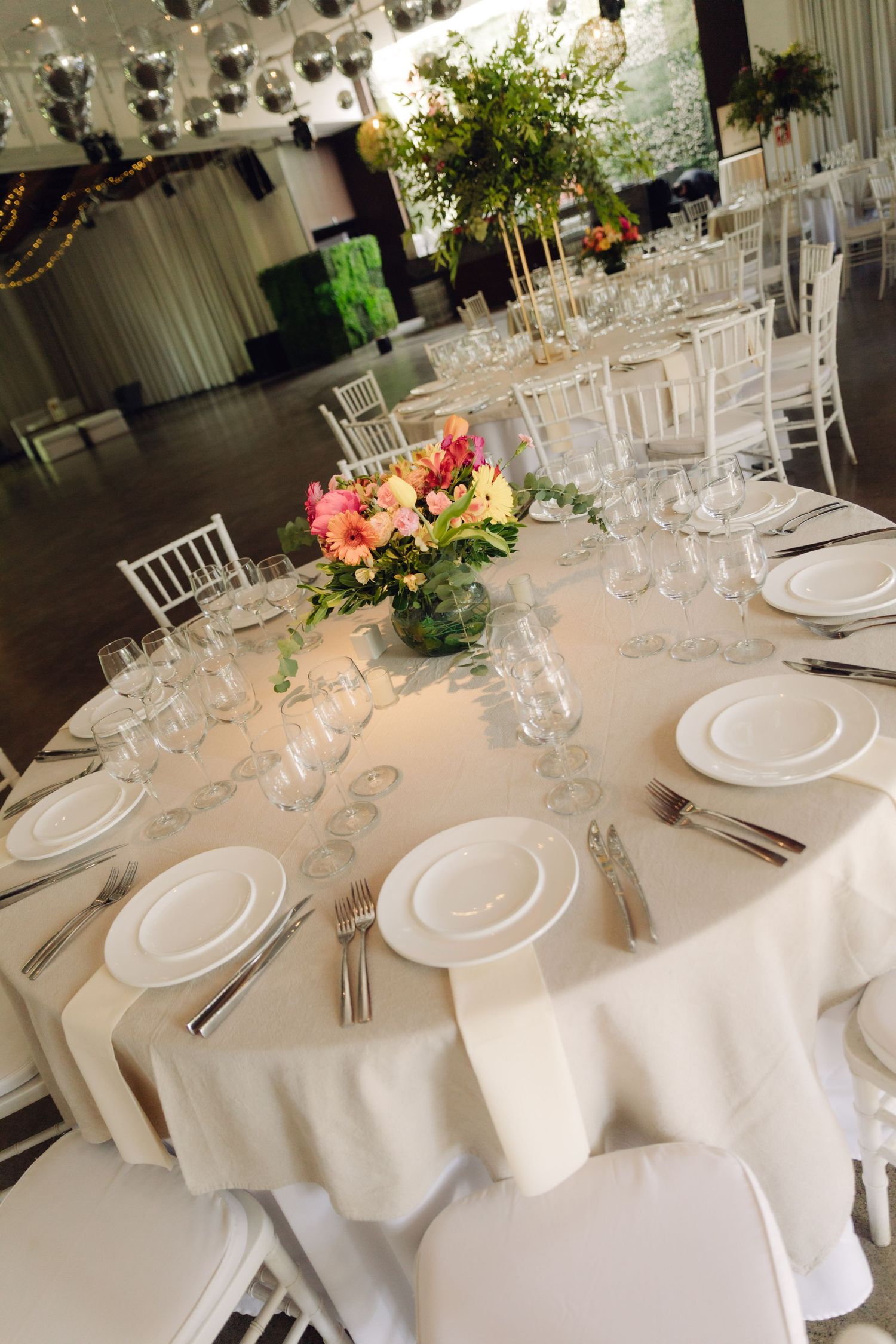 Elegant round wedding reception tables with white linens, crystal glasses, and pink floral centerpieces.