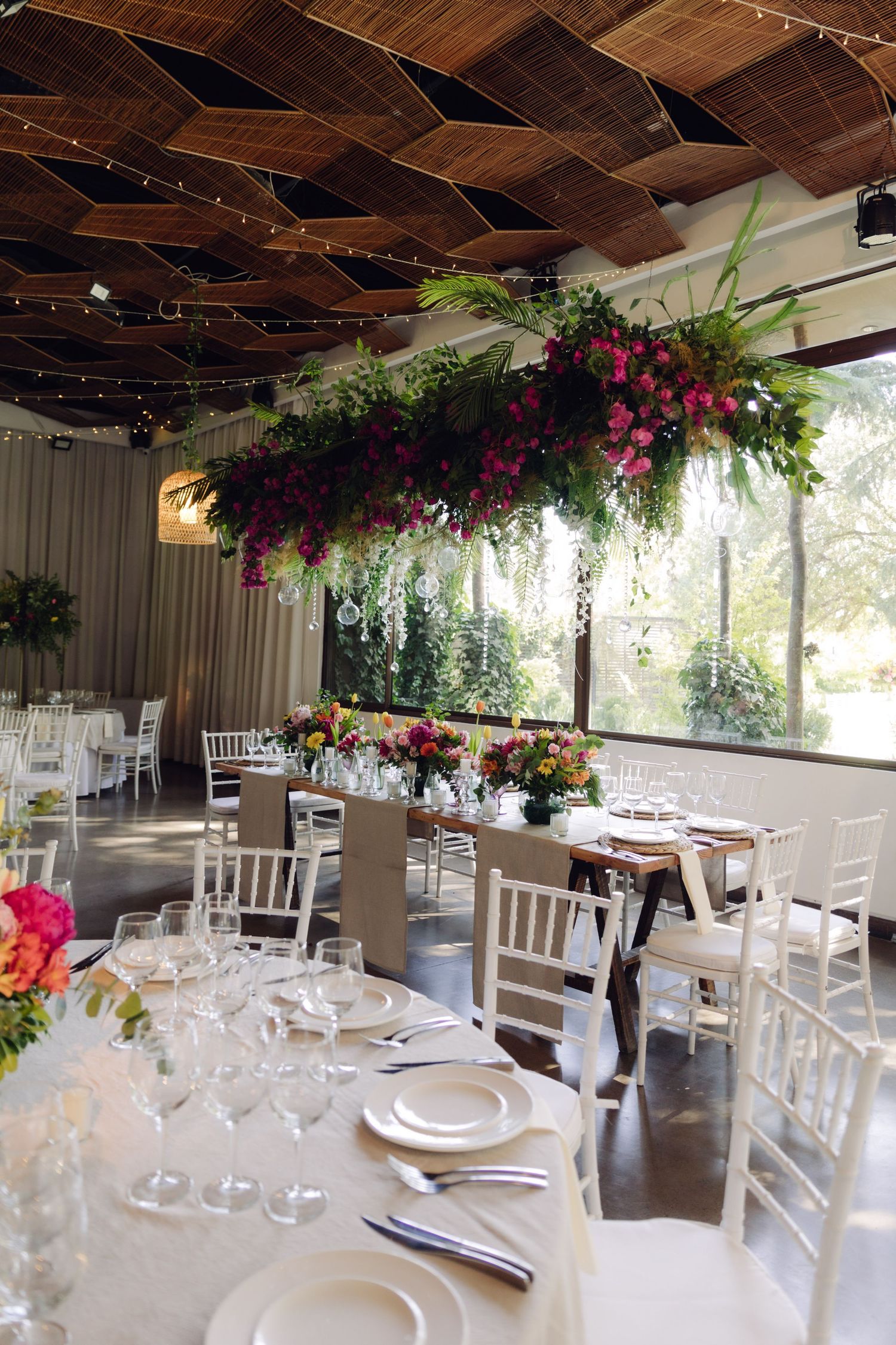 Stunning wedding venue with hanging floral installation, white Chiavari chairs, and string lights.
