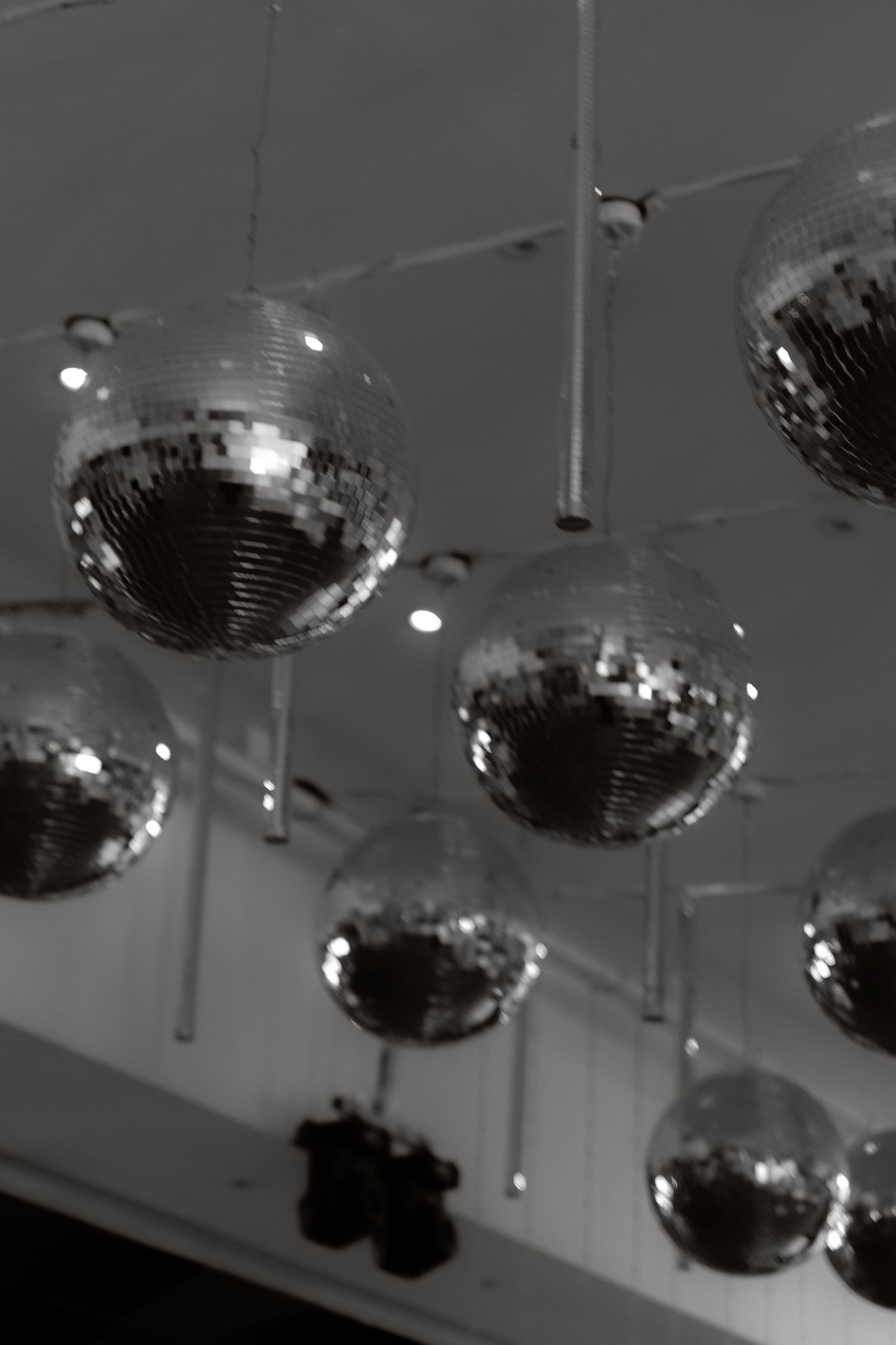 Multiple silver disco balls hanging from a white ceiling in a dark event venue.