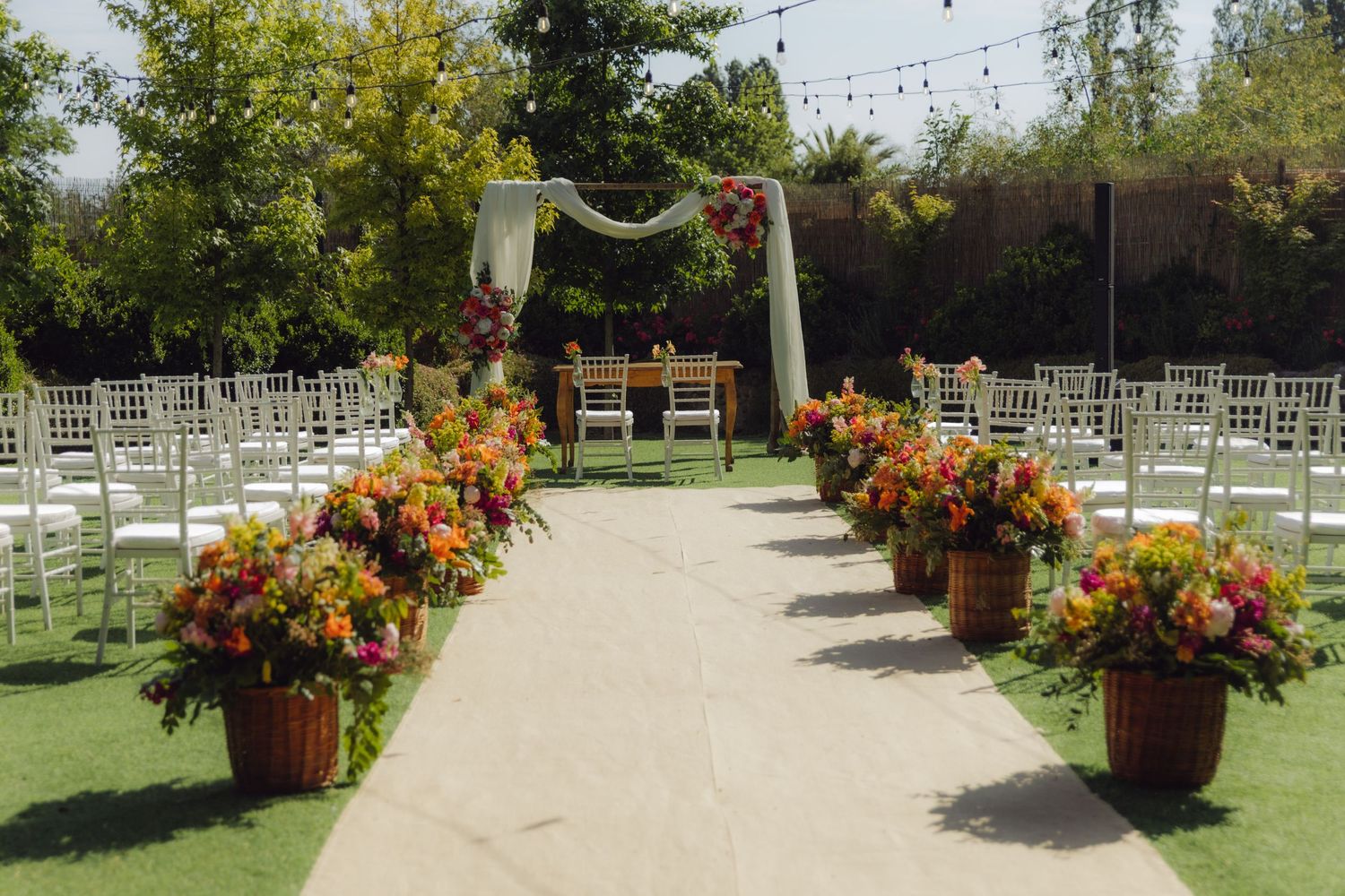 Elegant outdoor wedding ceremony aisle with colorful floral arrangements and white chairs.