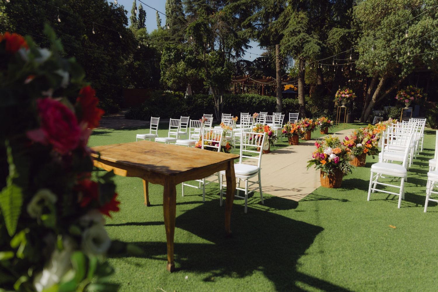 Rustic wooden table and white chairs arranged on green grass for an outdoor wedding ceremony.