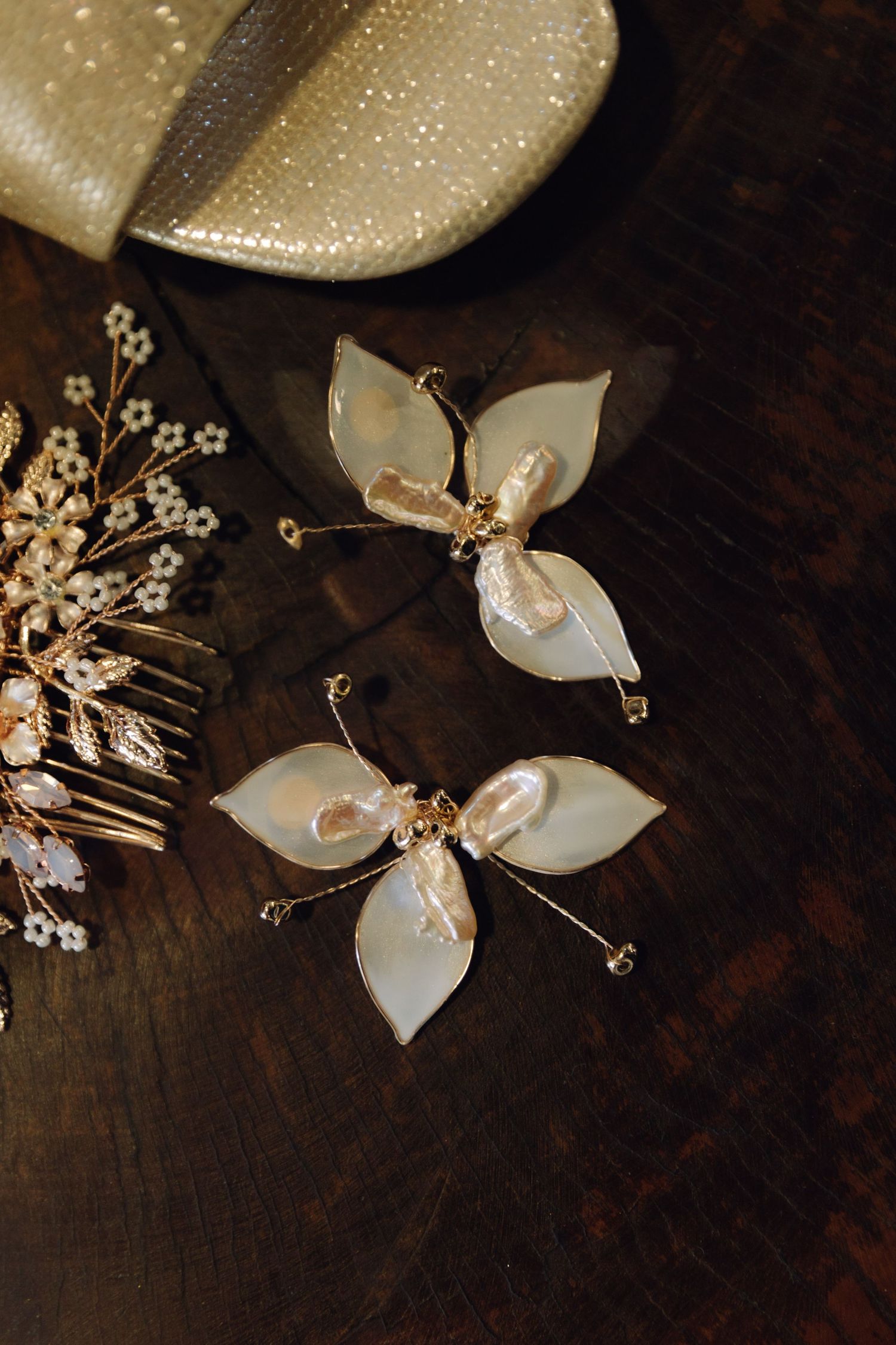 Delicate pearl and gold butterfly-shaped bridal earrings on a dark wooden surface.