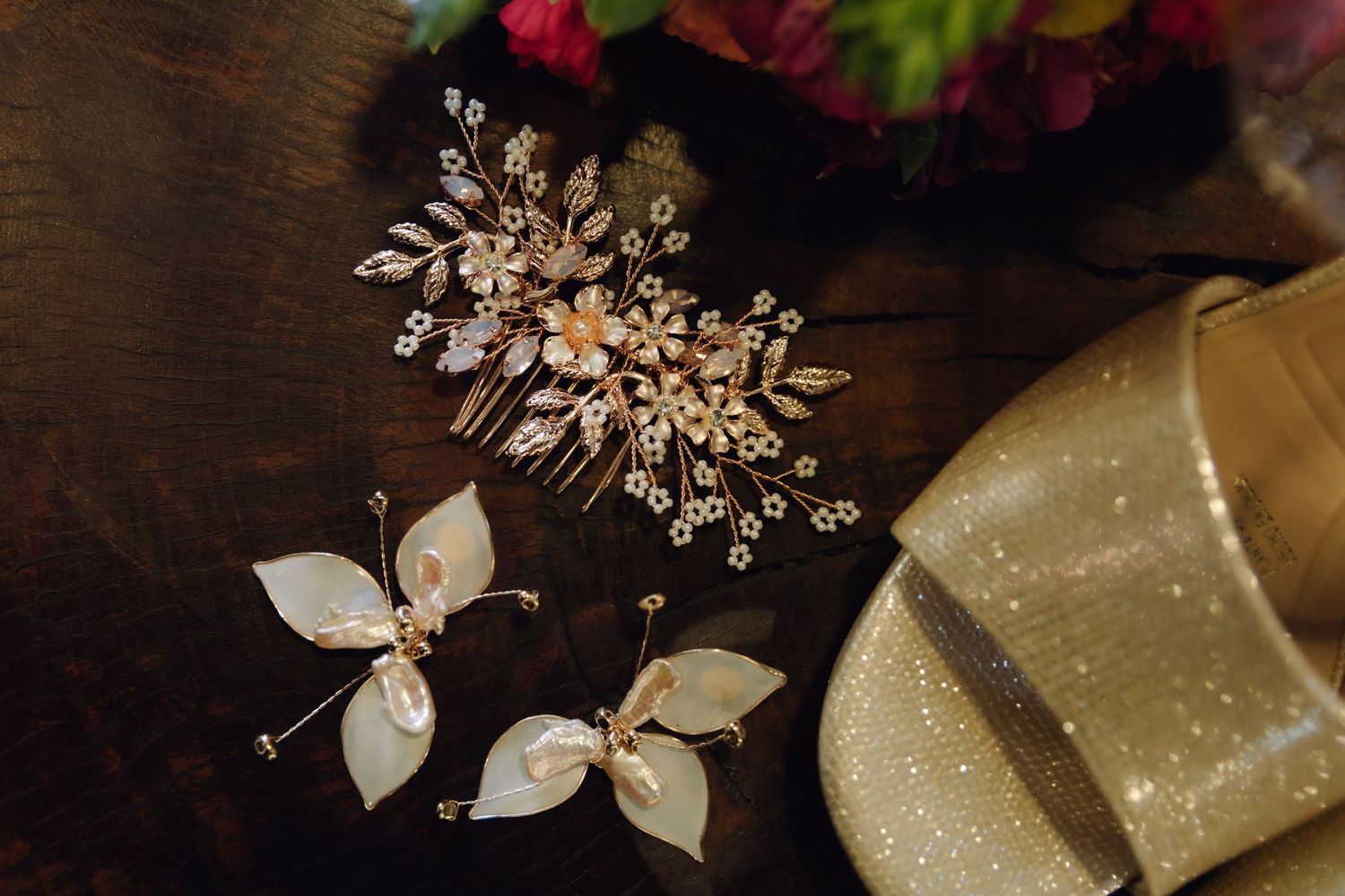 Ornate gold floral bridal hair comb and pearl butterfly earrings on a dark wood surface.