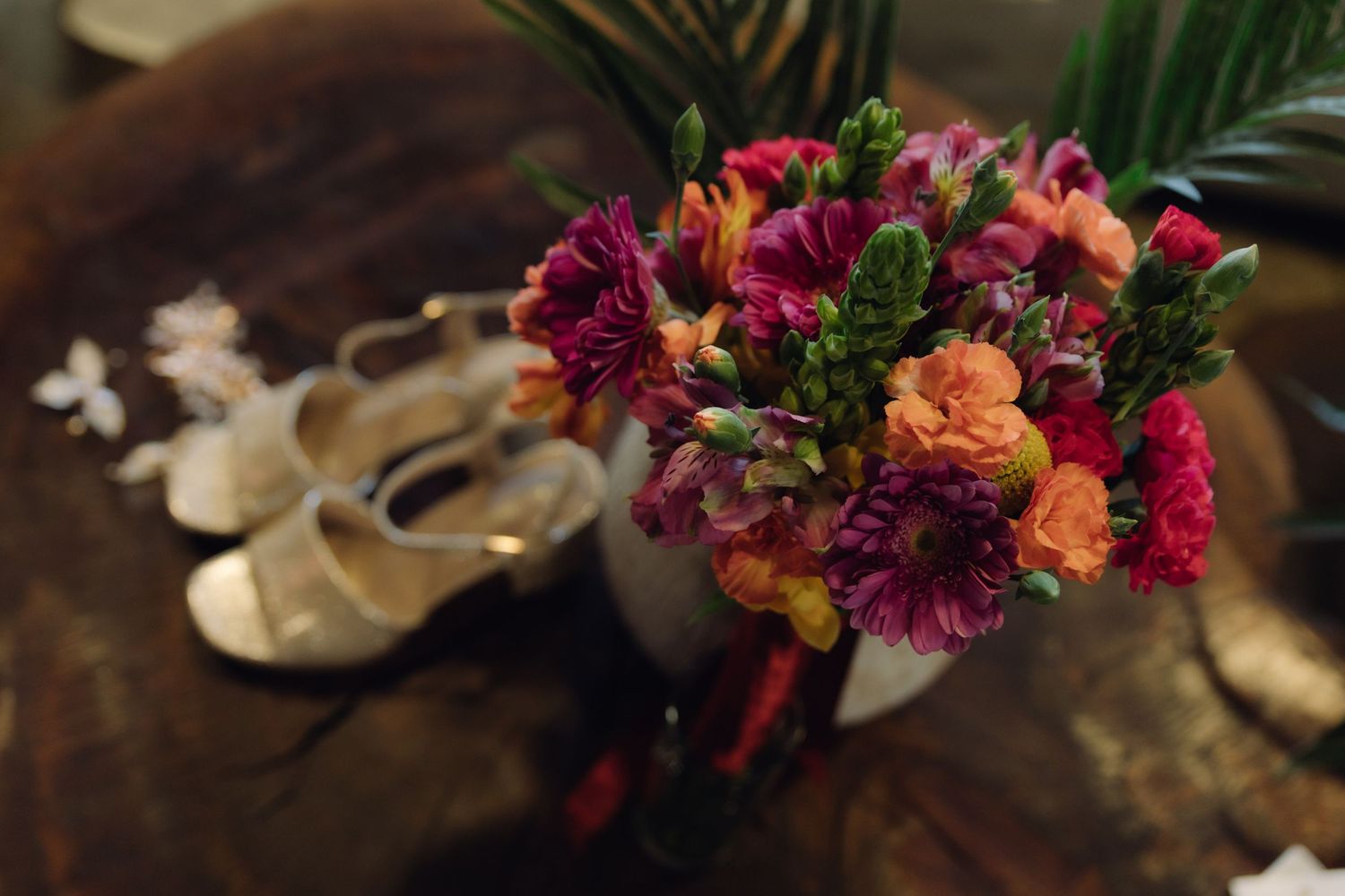 Vibrant bridal bouquet with pink, orange, and purple flowers beside gold wedding heels.