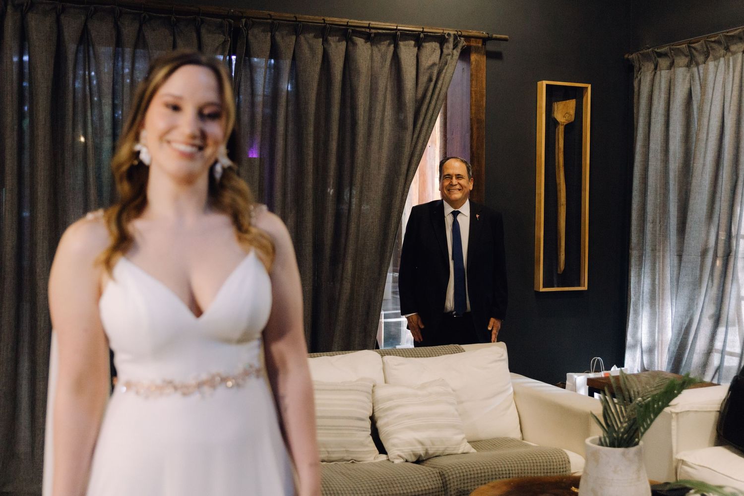 Bride in white gown smiles as father sees her for the first time before wedding ceremony.