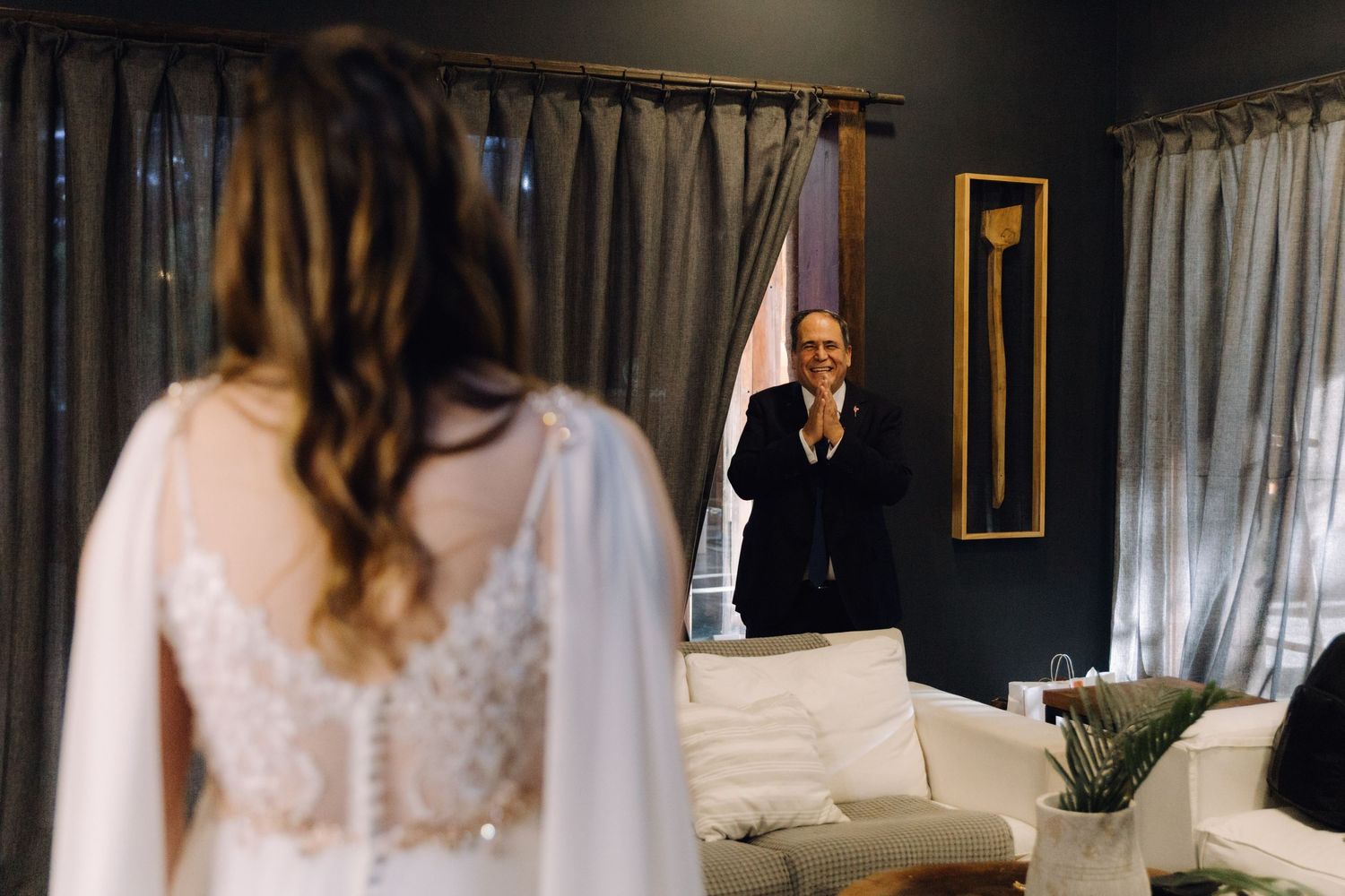 Father claps with joy during emotional first look as bride stands in lace wedding dress.