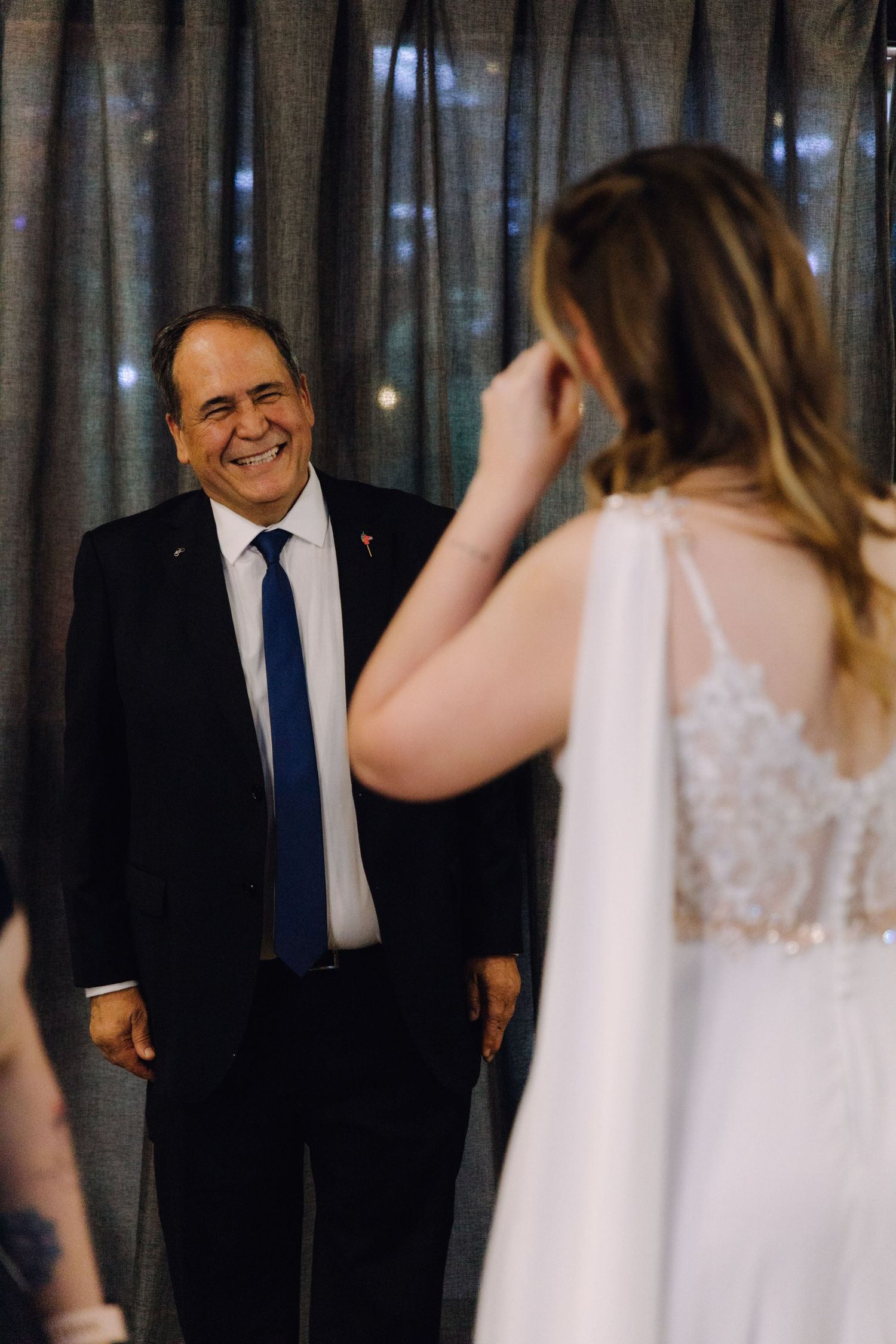 Proud father beams with happiness during first look reveal with bride in white gown.