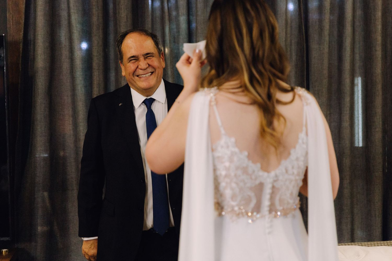 Father wipes tears of joy during emotional first look with bride in lace wedding dress.