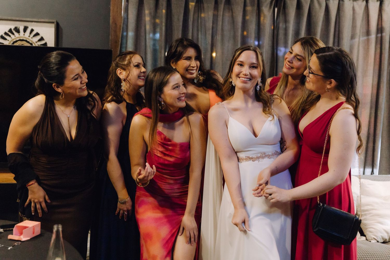 Bride laughs with bridesmaids dressed in vibrant red and mixed color formal gowns.