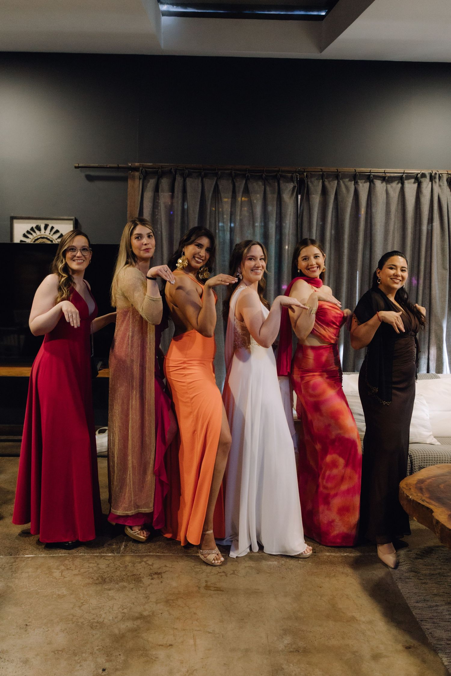 Bride and six bridesmaids in colorful gowns pose playfully before wedding celebration.