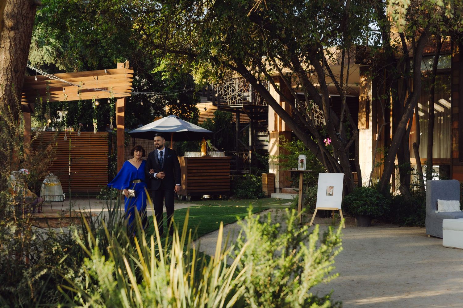 Couple in formal attire walking through a lush garden venue at a wedding celebration.