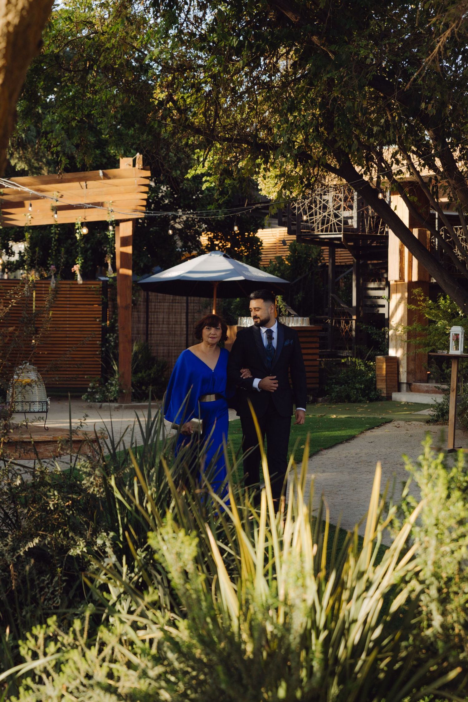 Elegant couple strolling through a beautifully landscaped outdoor wedding venue at golden hour.
