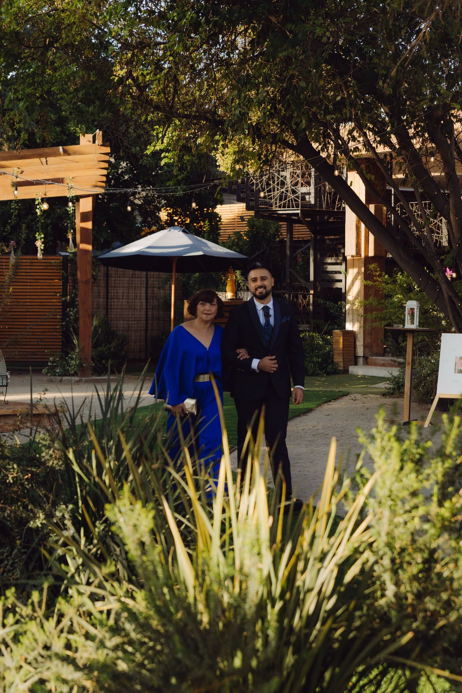Man in dark suit and woman in royal blue gown posing in a garden wedding venue.